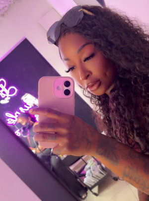 Woman with curly hair and tattoos taking mirror selfie in lit room.