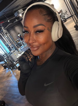 Woman with headphones taking selfie in gym wearing black top.