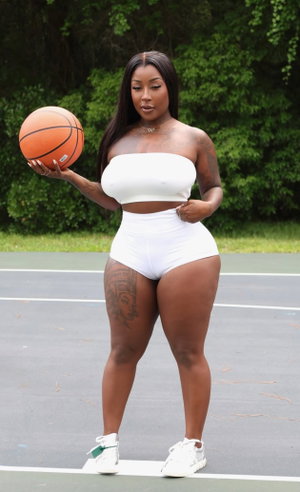Curvy woman in white top and shorts holding basketball on court.