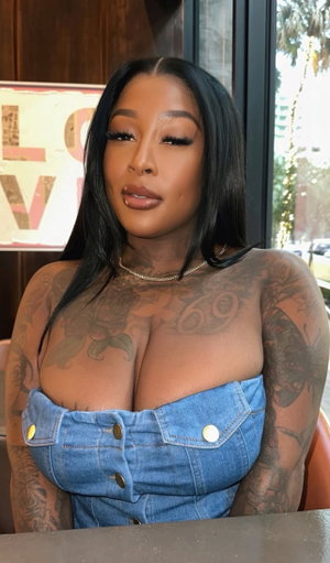 Tattooed woman with long black hair in denim top indoors.