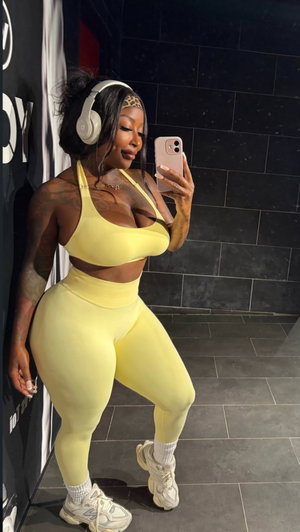 Curvy woman in yellow activewear taking mirror selfie indoors.
