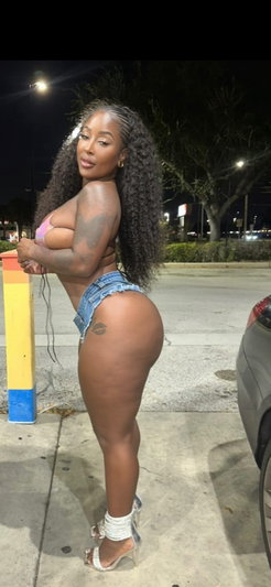 Woman with curly hair in denim shorts and a pink top, standing outdoors at night.