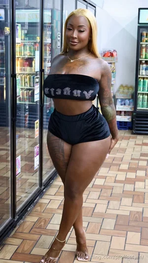 Woman with blonde hair and tattoos wears black bandeau top and shorts in a store.