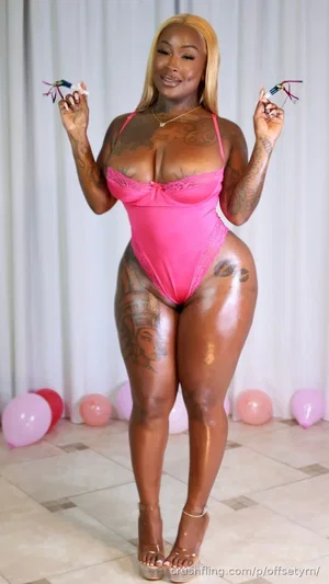 Woman in pink lace bodysuit with tattoos, standing indoors with balloons.