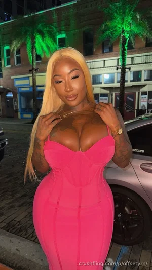 Woman with blonde hair in a pink dress, standing outdoors at night near a car and palm trees.