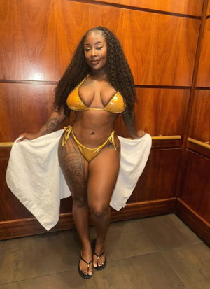 Curvy woman in yellow bikini holding towel in wooden indoor setting.