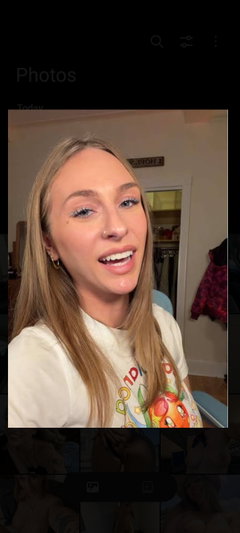 Woman with blonde hair wearing white graphic tee, indoors, smiling at camera.