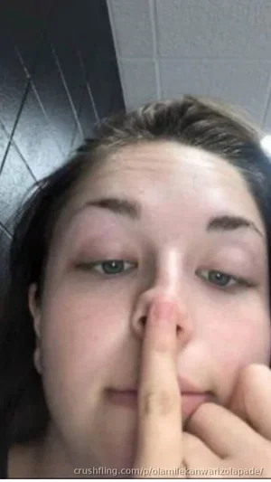 Woman with dark hair and green eyes touching nose with finger in close-up selfie.