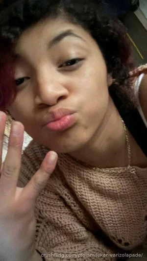 Woman with curly hair wearing a knitted top, making a playful face in a close-up selfie.
