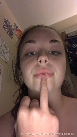 Woman with bare shoulders and finger on lips, indoors, close-up selfie.