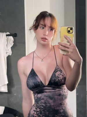 Red-haired woman in patterned dress taking bathroom mirror selfie.