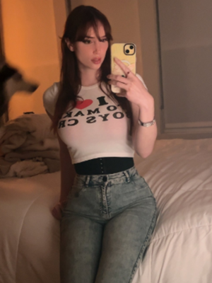 Brunette woman in crop top and jeans taking bedroom selfie.