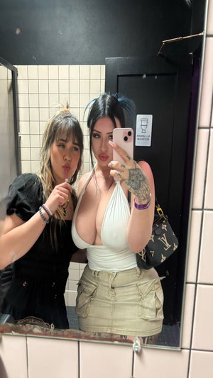 Two curvy women in bathroom mirror selfie, one in white halter top and skirt.