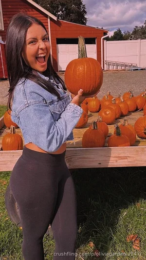 Woman in denim crop top and leggings holding pumpkin at outdoor farm stand.