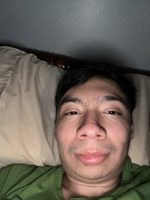 Man in green shirt lying on bed with pillow.