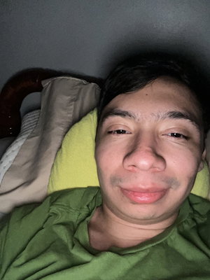 Man in green shirt lying on bed with yellow pillow.