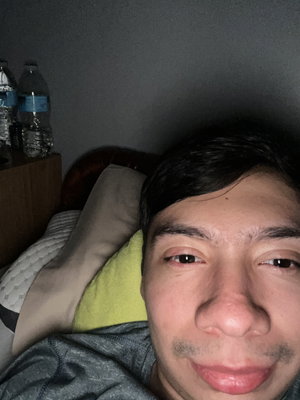 Asian man with dark hair in gray shirt lying in bed.