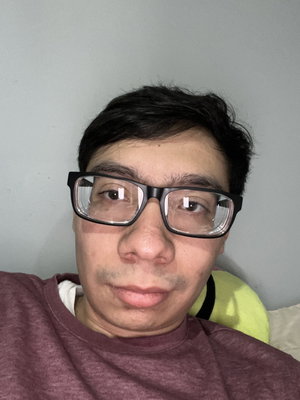 Man with glasses in maroon shirt reclining indoors.