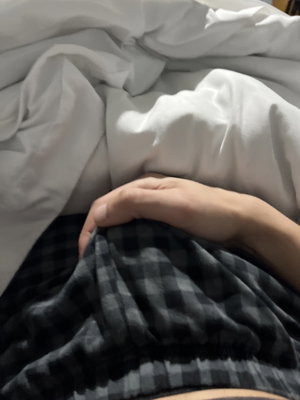 Hand resting on checkered pants under white sheets in bed.