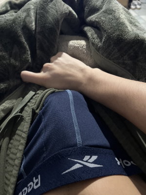 Person in blue underwear and green pants under gray blanket, hand resting on lap.