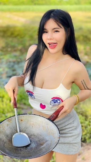 Curvy asian woman in white top outdoors holding wok.
