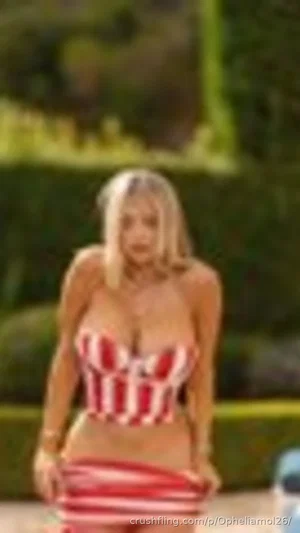 Blonde woman in red and white striped bikini top and skirt, standing outdoors.