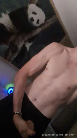 Shirtless man in black pants, standing indoors near panda artwork.