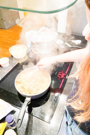 Woman with long hair cooking in kitchen, wearing jeans and dark top.