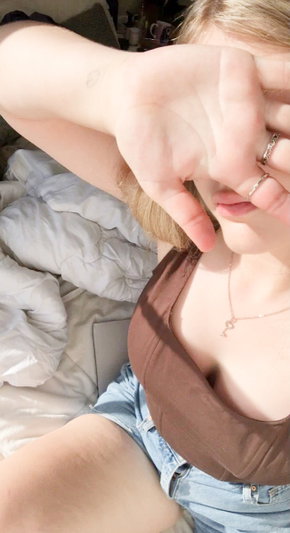 Blonde woman in brown top and shorts taking selfie in bedroom.