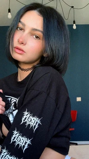 Woman with short dark hair in black graphic tee, indoors, facing camera.