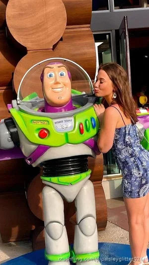 Woman in blue patterned dress posing with Buzz Lightyear statue outdoors.