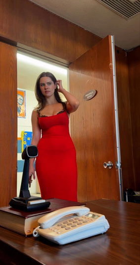 Woman in red dress with black lace straps standing in doorway, hand near hair.