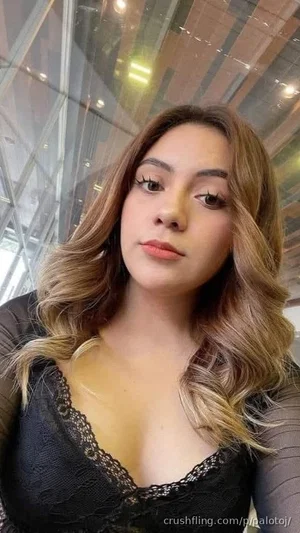 Woman with wavy hair in black lace top, indoors near glass wall.