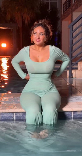 Woman in mint green bodysuit sitting at pool edge at night.