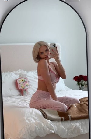 Blonde woman in pink lingerie taking mirror selfie on bed