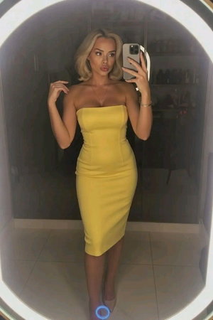 Woman in yellow strapless dress taking mirror selfie indoors.