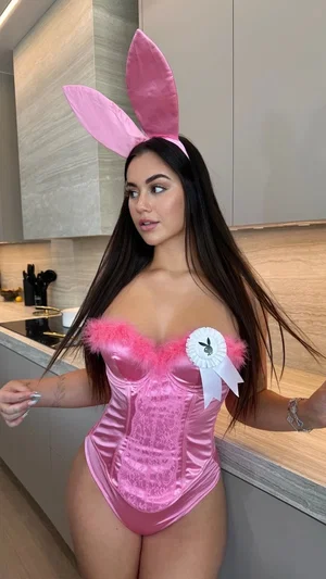 Woman in pink bunny costume with corset top and ears in kitchen.