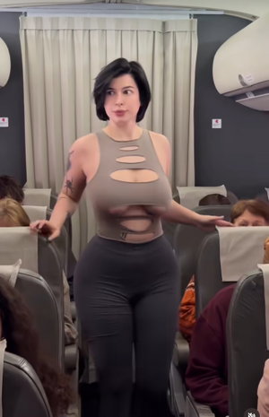 Woman in cutout top and leggings standing in airplane cabin.
