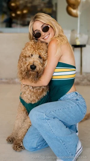 Blonde woman in striped top and jeans hugging a fluffy dog indoors.