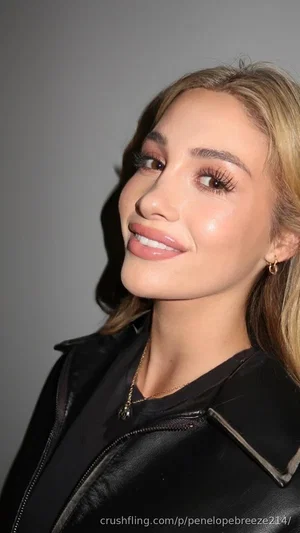 Woman with blonde hair wearing black leather jacket, smiling, studio setting.