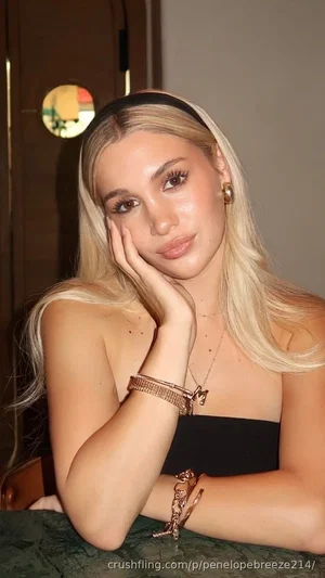 Blonde woman in black strapless top, resting hand on cheek, indoor setting.