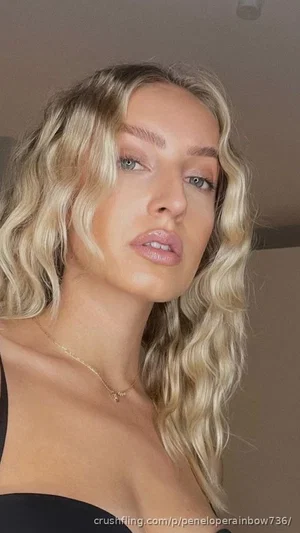 Blonde woman with wavy hair wearing black top, indoors, close-up selfie.