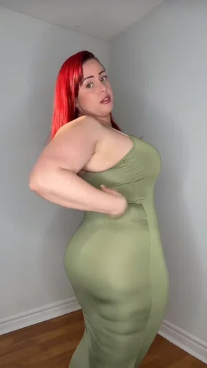 Woman with red hair in green dress posing indoors.