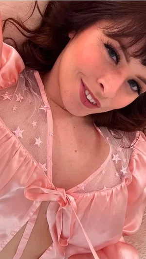 Woman in pink star-patterned sheer lingerie, lying down, smiling at camera.