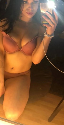 Woman in pink lingerie posing in mirror selfie, indoor setting.