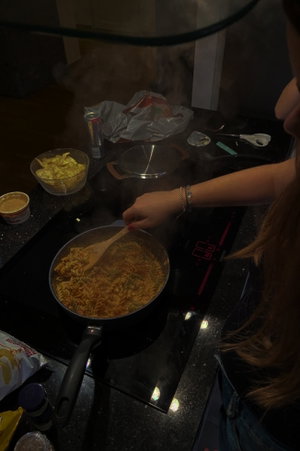 Woman with long hair cooking pasta on stovetop in kitchen, wearing jeans.
