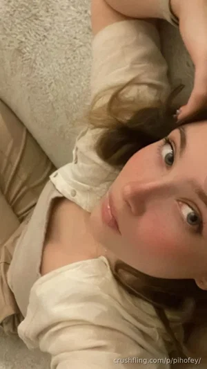 Woman with light brown hair lying on a beige couch, wearing a white button-up shirt.