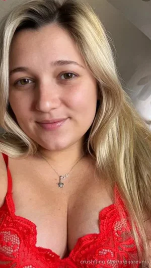 Woman with blonde hair wearing red lace lingerie, indoor selfie.