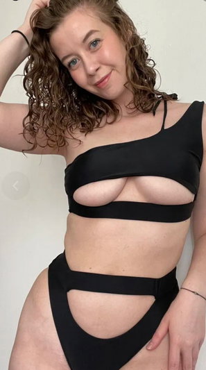 Woman with curly brown hair in black cutout outfit indoors.