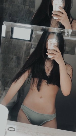 Slim Asian woman in black bra and green panties in bathroom mirror.